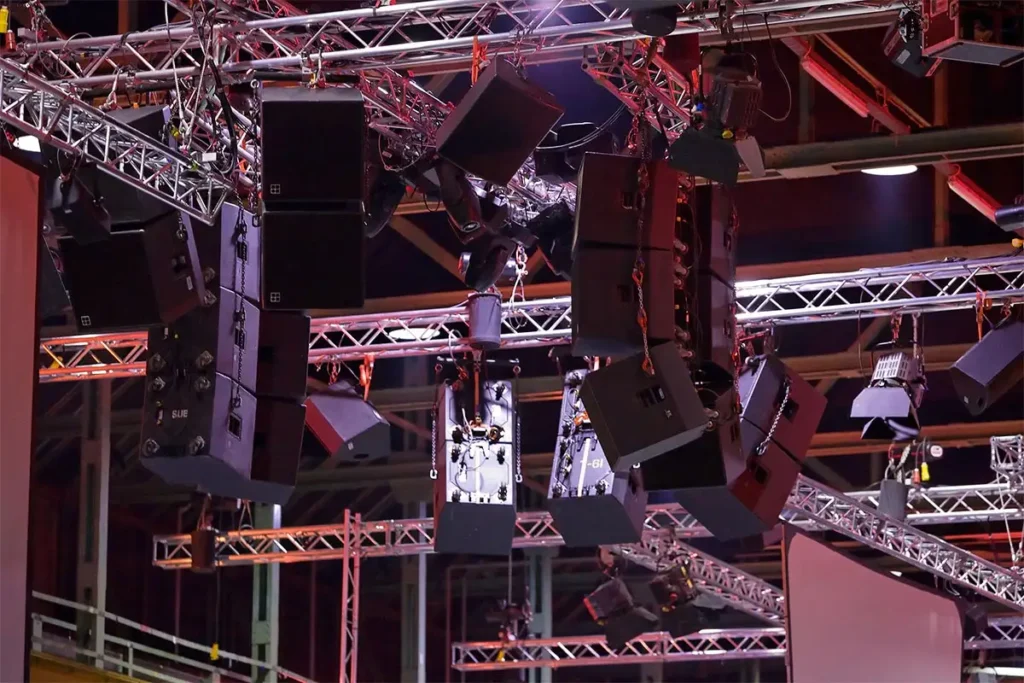 Professionelle Veranstaltungstechnik in Ergolding mit mehreren Line-Array-Lautsprechern und Lichtsystemen an Traversenstruktur in einer Messehalle.
