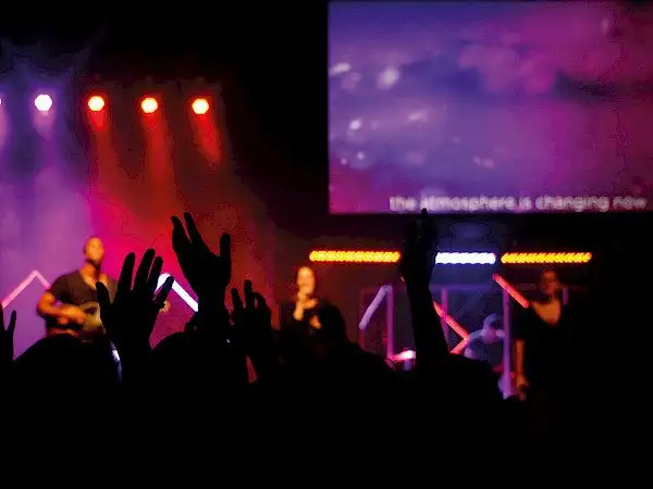 Eine Menschenmenge bei einem Konzert, ausgestattet von Orange Veranstaltungstechnik Kirchheim bei München, hebt euphorisch die Hände.